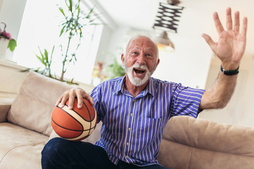 Senior man cheering for a basketball game and holding a basketball ball