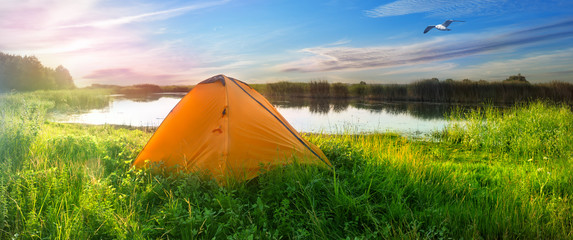 Orange tent on the shore of the lake © alexlukin