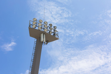 Sports stadium floodlight tower with reflectors with blue sky.