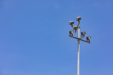 Sports stadium floodlight tower with reflectors with blue sky.