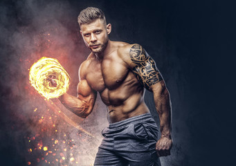 Fototapeta na wymiar Handsome shirtless tattooed bodybuilder with stylish haircut and beard, wearing sports shorts, posing in a studio. Fire art concept.