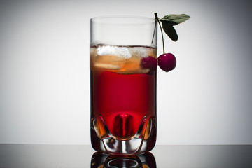 Homemade fresh cherry juice in transparent glass with ice and fresh cherry. Gradient background.
