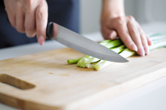 Female hands with a knife, slicing vegetables on a wooden board on a white background.