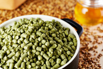 English hops granulated in a clay dish. Spilled barley malt and  jar of honey in the background.