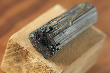 Black tourmaline stone on a background of natural wood American black walnut. Mineral collection...