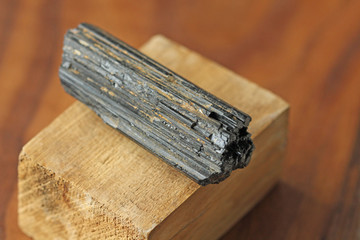 Black tourmaline stone on a background of natural wood American black walnut. Mineral collection...