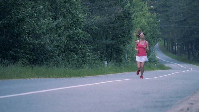 Good-looking lady is jogging along the road in the forest