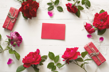 Red roses flowers and red empty card for your text on a white wood background, top view. 
