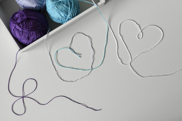 View from above on creative designed hearts from colorful wool strands coming out of the white box with knitting yarn balls.