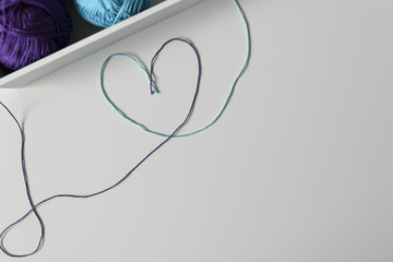 Knitting wools strands used in a creative way to design colorful heart symbol on white background with copy space.
