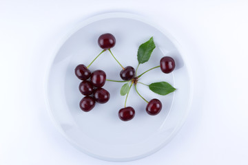 Red cherries on a white plate, fresh cherries with green leaves, red berries in the style of minimalism, vegetarian food, blank for the designer, isolated