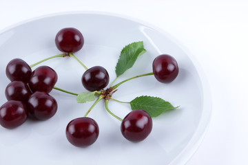 Red cherries on a white plate, fresh cherries with green leaves, red berries in the style of minimalism, vegetarian food, blank for the designer, isolated