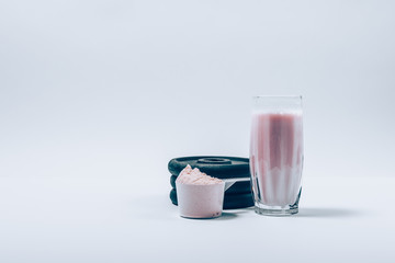 Whey protein shake in glass next to scoop of powder