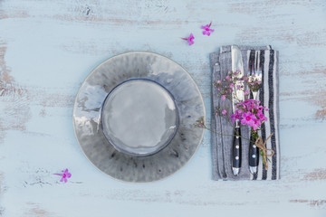 Rustic table setting with pink flowers on light wooden table.
