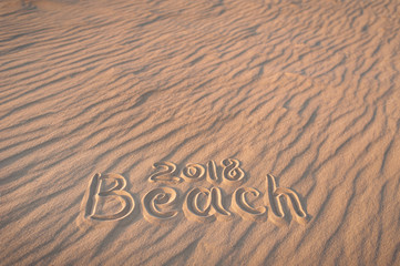 Fototapeta na wymiar The inscription on the sand. The beach of 2018. The word beach is written on the sand by hand. Beach season. Postcard. Shadows on the sand.