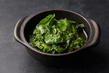 Basil pesto sauce with parmesan cheese, nuts, olive oil and garlic in black cast iron mortar, close up view