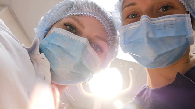 Smiling dentist and the assistant in glasses have bent over the patient and treat a teeth