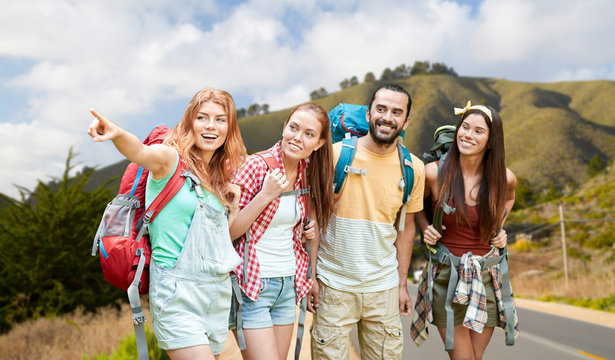 adventure, travel, tourism, hike and people concept - group of smiling friends with backpacks pointing finger over big sur hills of california background