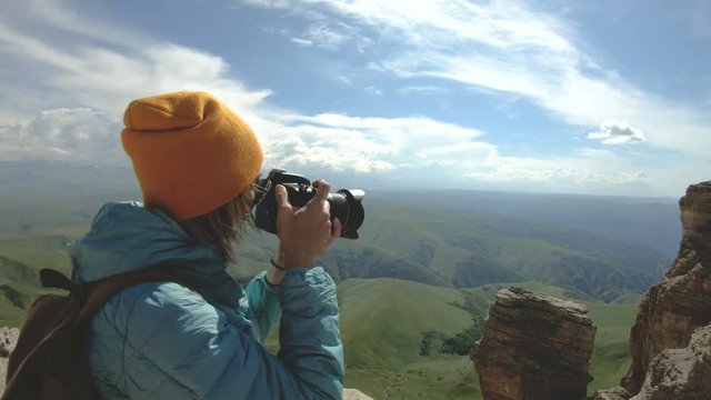 Blonde girl photographer in the cap takes a photo on her digital camera with a background of rocks in the Caucasus
