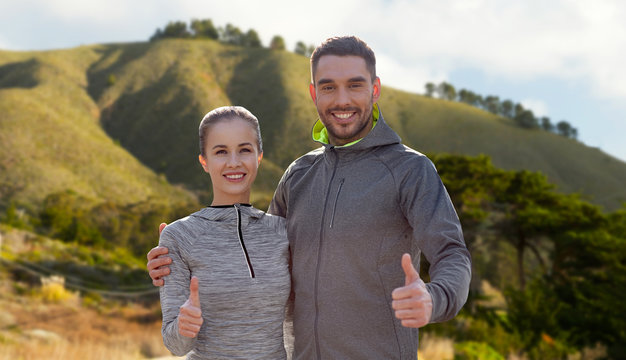 fitness, sport and gesture concept - smiling couple outdoors showing thumbs up over big sur hills background in california
