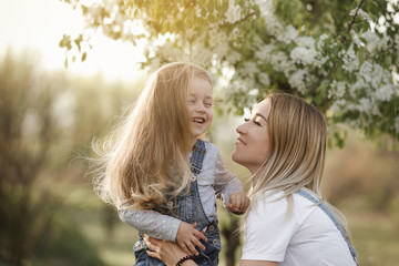 young mother with adorable daughter in park with blossom tree