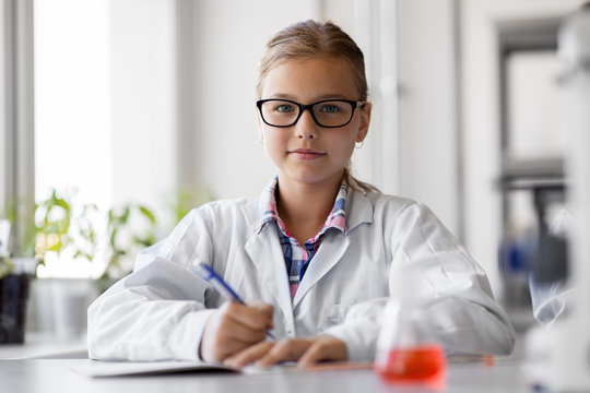 education, science and children concept - girl studying chemistry at school laboratory and writing to workbook