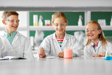 education, science, chemistry and children concept - kids or students with test tube making...