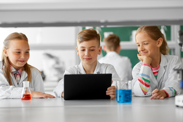 education, science and technology concept - kids with tablet pc computer studying chemistry at school laboratory