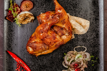 roasted chicken legs on a black plate, decorating a chili pepper, onion and fried garlic