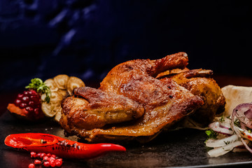 roasted chicken legs on a black plate, decorating a chili pepper, onion and fried garlic