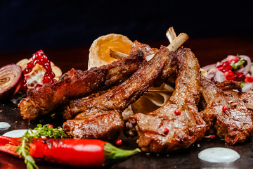 rack of lamb on a black plate decorated with pepper, pomegranate, onion and garlic