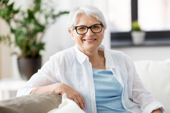 vision, age and people concept - portrait of happy senior woman in glasses sittin on sofa at home