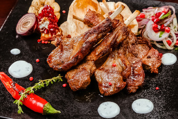 rack of lamb on a black plate decorated with pepper, pomegranate, onion and garlic