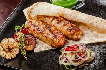 lulia kebab on a black plate with sauce. Decoration of onions, rosemary and garlic