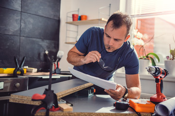 Man checking blueprints while building kitchen cabinets