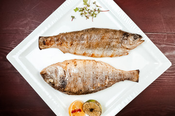 Fried fish on a wooden background. With lemons and spices.