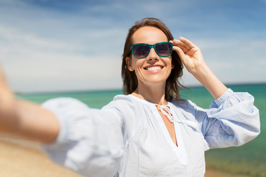 summer holidays and leisure concept - happy smiling woman in sunglasses taking selfie on beach