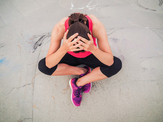 worried and desperate woman after fitness workout in sportswear from bird view on grey cement background