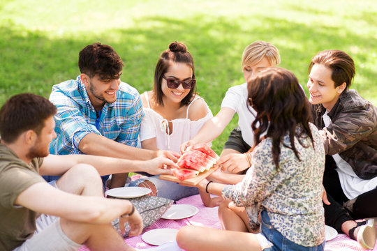 friendship, leisure and summer concept - group of happy friends eating watermelon at picnic in park