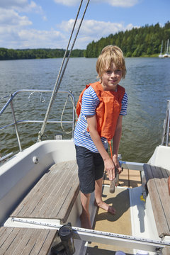  Child boy holding a yacht rudder. Cute boy captain on board of sailing yacht on summer cruise. Travel adventure, yachting with child on family vacation.