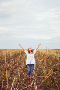 Young blond girl in casual clothes with arms raised enjoys her walking in field.
