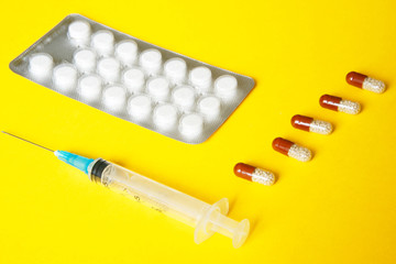 Health problems. Blister with white tablets, capsules with granules and a syringe lie on a yellow background.
