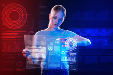 Transparent gadget. Calm clever teenage girl carefully holding a transparent device and touching the icons on the screen of it while preparing her school project