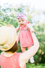 Beautiful Mother with the straw hat And her little daughter outdoors family look in in a pink dress . Young mother throws up baby in the sky, on sunny day.