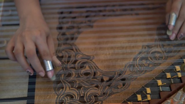 Fingers playing and plucking the strings of a qanun.