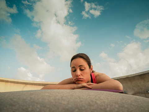 Unmotivated And Groggy Sporty Woman After Fitness Workout With Blue Cloudy Sky In The Background