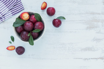 Fresh plums with leaves on rustic wooden table background.