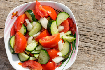 Fresh vegetable salad  with tomatoes, cucumbers, onion and olive oil on wooden table. Top view