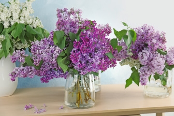 Vases with beautiful blossoming lilac on table against light background. Spring flowers