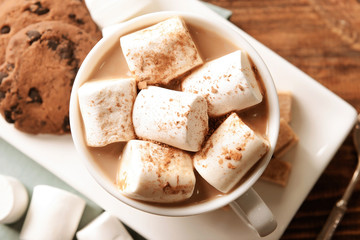 Cup of delicious cocoa drink with marshmallows and cookies on plate, top view